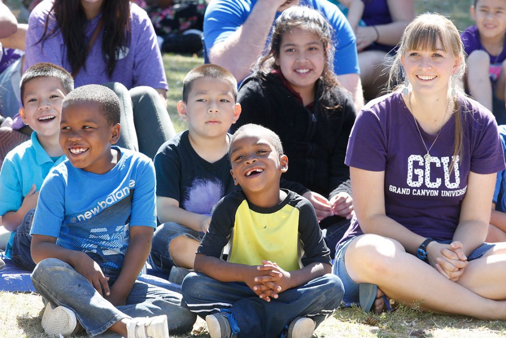 GCU volunteer with young students smiling outside